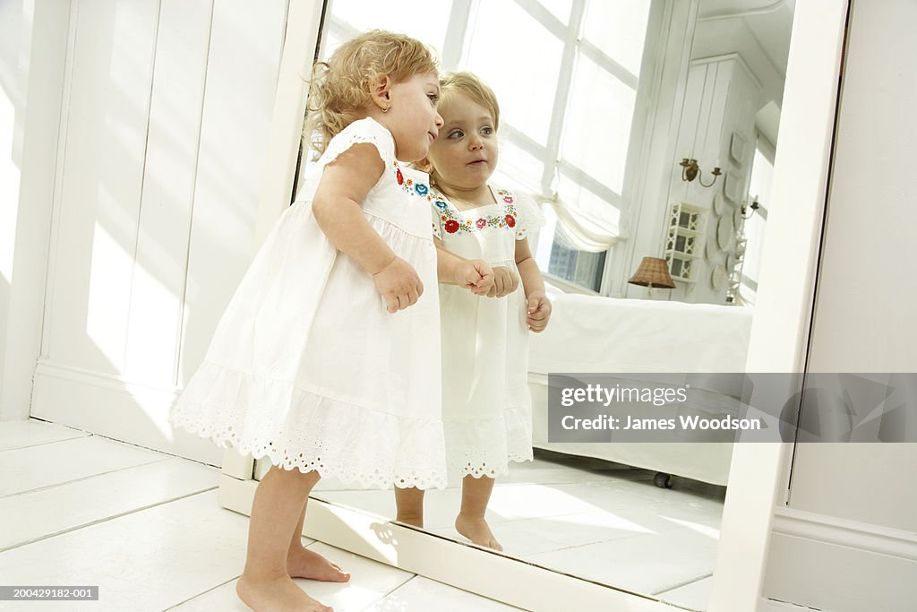 Baby girl (18-24 months) looking in mirror, side view