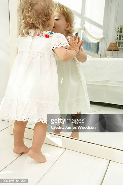 baby girl (18-24 months) looking in mirror, hands pressed on glass - james blondes stockfoto's en -beelden