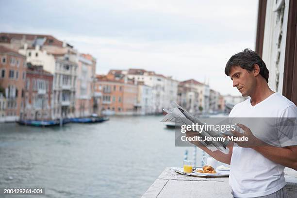 italy, venice, man reading newspaper on balcony by breakfast tray - balcony reading stock pictures, royalty-free photos & images