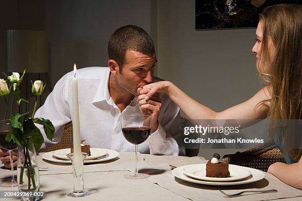 man kissing back of woman's hand at candlelit dinner - mesa para dos fotografías e imágenes de stock