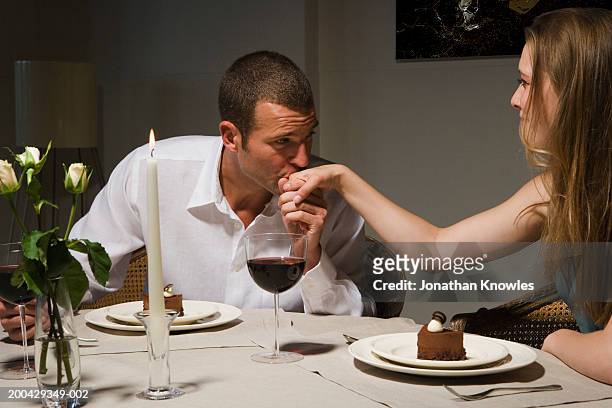 man kissing back of woman's hand at candlelit dinner - tafel voor twee stockfoto's en -beelden