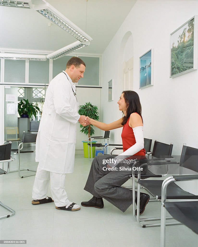 Doctor shaking hands with female patient with arm in cast, side view