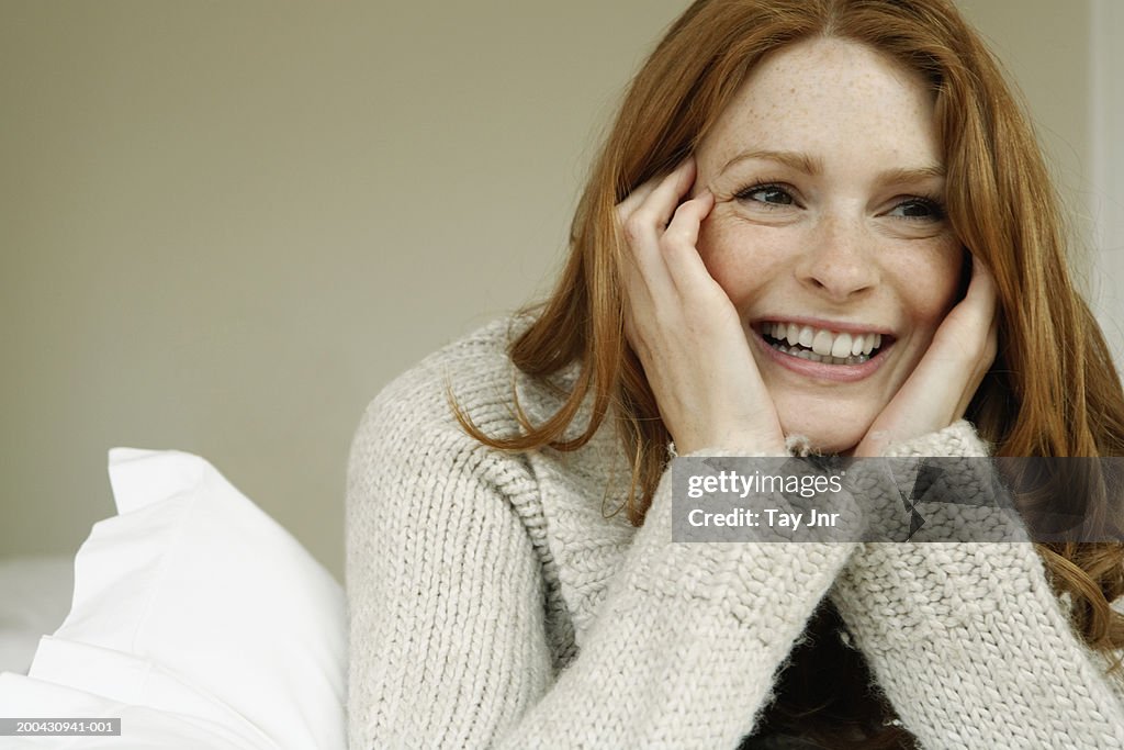 Young woman lying on bed, resting head in hands, laughing, close-up