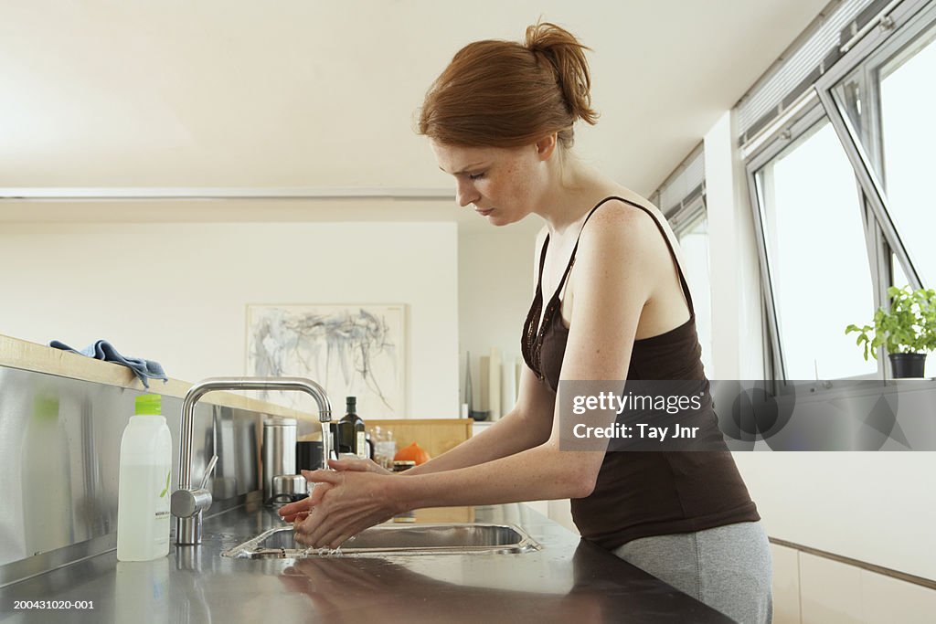 Young woman washing hands at kitchen sink, side view