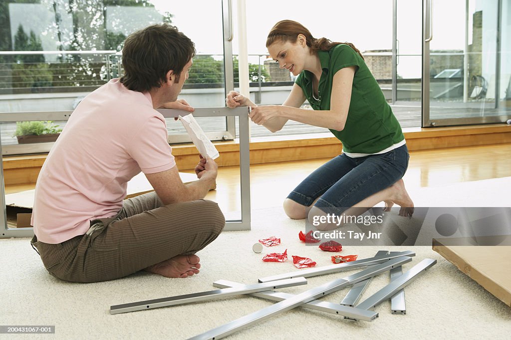 Young couple assembling flat-pack furniture, side view
