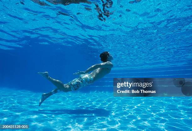 young man simming underwater in pool, underwater view - agua estancada fotografías e imágenes de stock