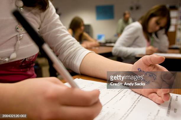 teenage girl (15-17) cheating on math test (focus on formula on hand) - build presents the cast of liar stockfoto's en -beelden