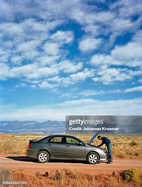 man looking under hood of car on desert road, side view - car side by side stock pictures, royalty-free photos & images