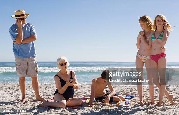 three generational family on beach, three using mobile phones - old woman in swimsuit stock-fotos und bilder