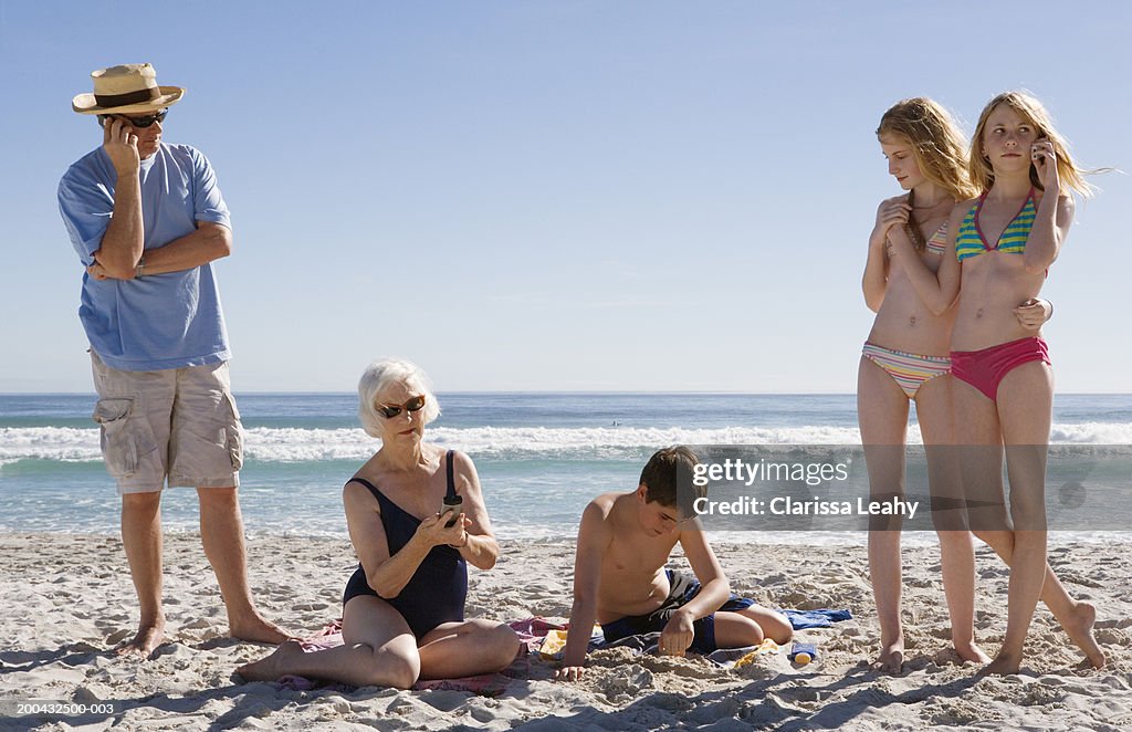 Three generational family on beach, three using mobile phones