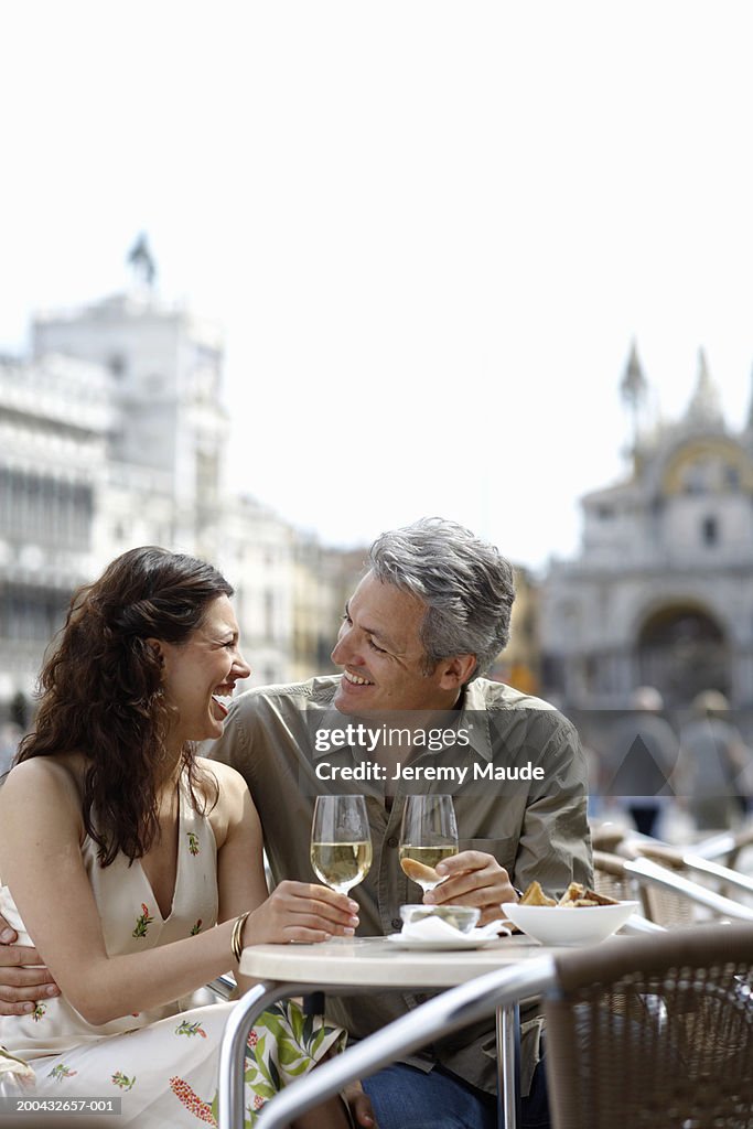Italy, Venice, couple drinking wine at cafe table, laughing
