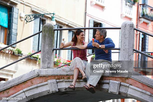 italy, venice, couple sitting on bridge holding ice cream cones - venice italy stock-fotos und bilder