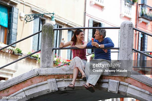 italy, venice, couple sitting on bridge holding ice cream cones - venice italy bildbanksfoton och bilder
