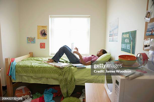 young woman lying on bed using laptop computer, in student dormitory - dorm room stock pictures, royalty-free photos & images