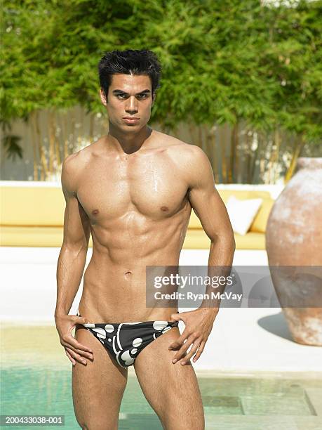young man in racing briefs standing beside pool, hands on hips - young men in speedos stock-fotos und bilder