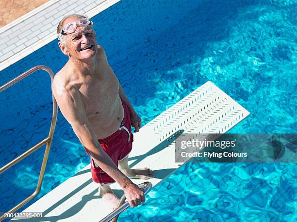 senior man standing on diving board, smiling, portrait, overhead view - zwembroek stockfoto's en -beelden