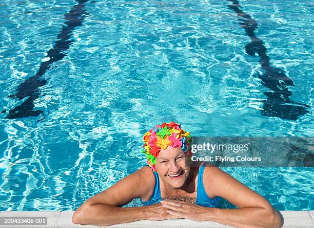 senior woman wearing swimming hat, resting on edge of pool, smiling - cuffia da nuoto foto e immagini stock