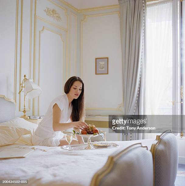 young woman eating fruit on bed - premium paris stock pictures, royalty-free photos & images