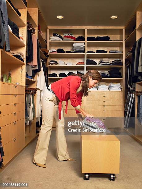 woman laying folded clothing on bench in walk-in closet - armadio a muro foto e immagini stock