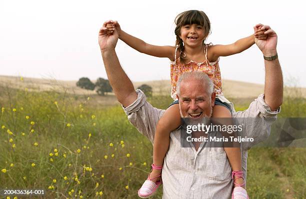 girl (4-6) sitting on grandfather's shoulders, smiling, portrait - llevar al hombro fotografías e imágenes de stock