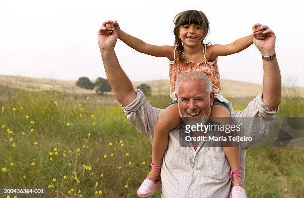 girl (4-6) sitting on grandfather's shoulders, smiling, portrait - granddaughter stock pictures, royalty-free photos & images