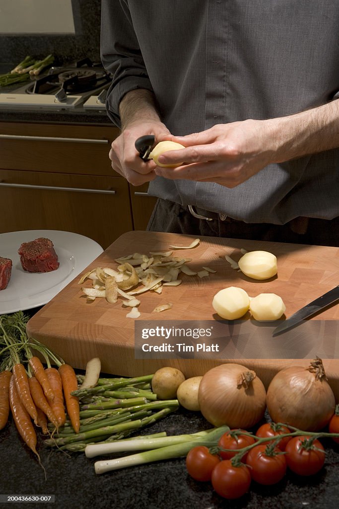 Man peelinig potatoes above cutting board in kitchen, close-up