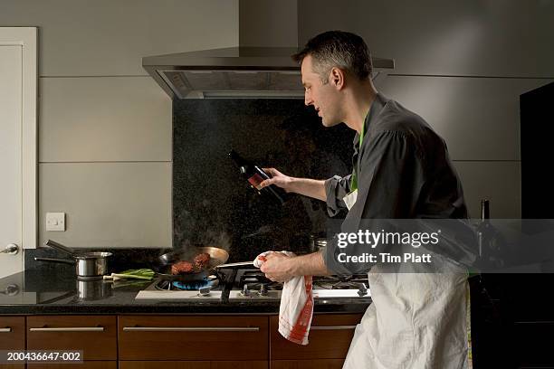 man with bottle of wine tilting pan on stove, side view - cooking apron stock pictures, royalty-free photos & images