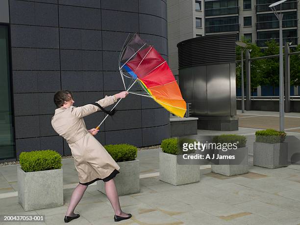 businesswoman holding onto umbrella turned inside out in wind - struggle stock pictures, royalty-free photos & images