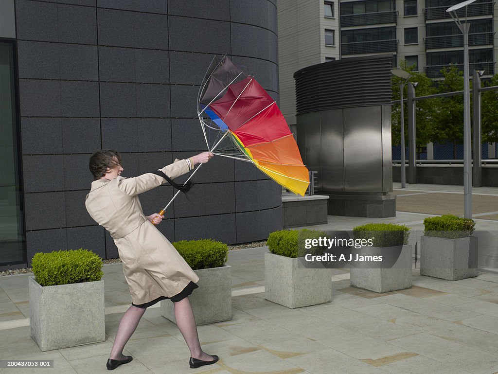 Businesswoman holding onto umbrella turned inside out in wind