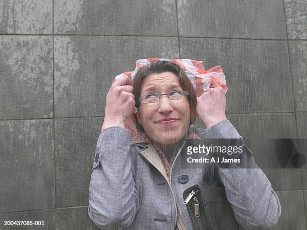 businesswoman standing in rain holding plastic bag over head, close-up - sheltering stock-fotos und bilder