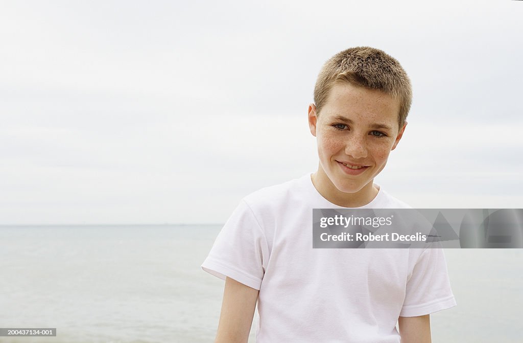 Boy (11-13) standing on beach, smiling, portrait