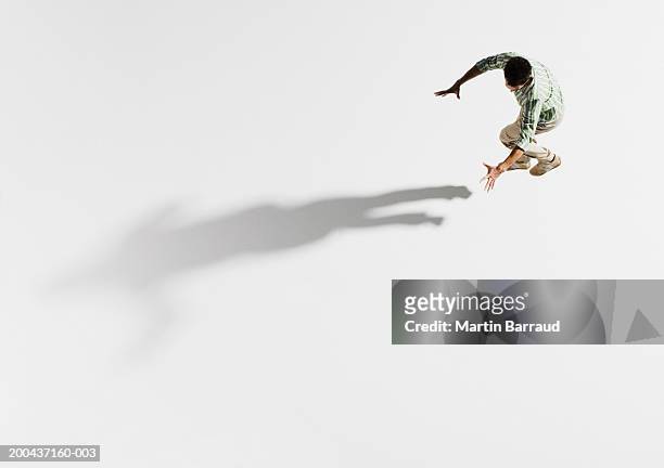young man jumping, holding arms out towards shadow, overhead view - elevated view of person on white background stock pictures, royalty-free photos & images
