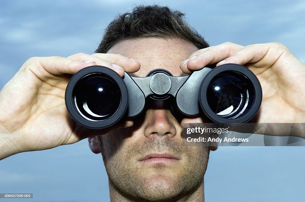 Man looking through binoculars outdoors, close-up