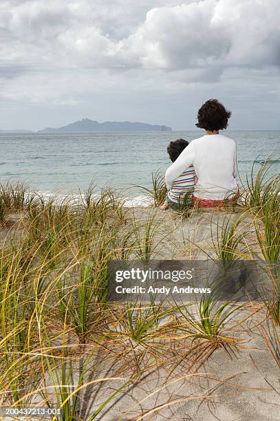 mother and son (2-4) sitting on beach, rear view - medelavstånd bildbanksfoton och bilder