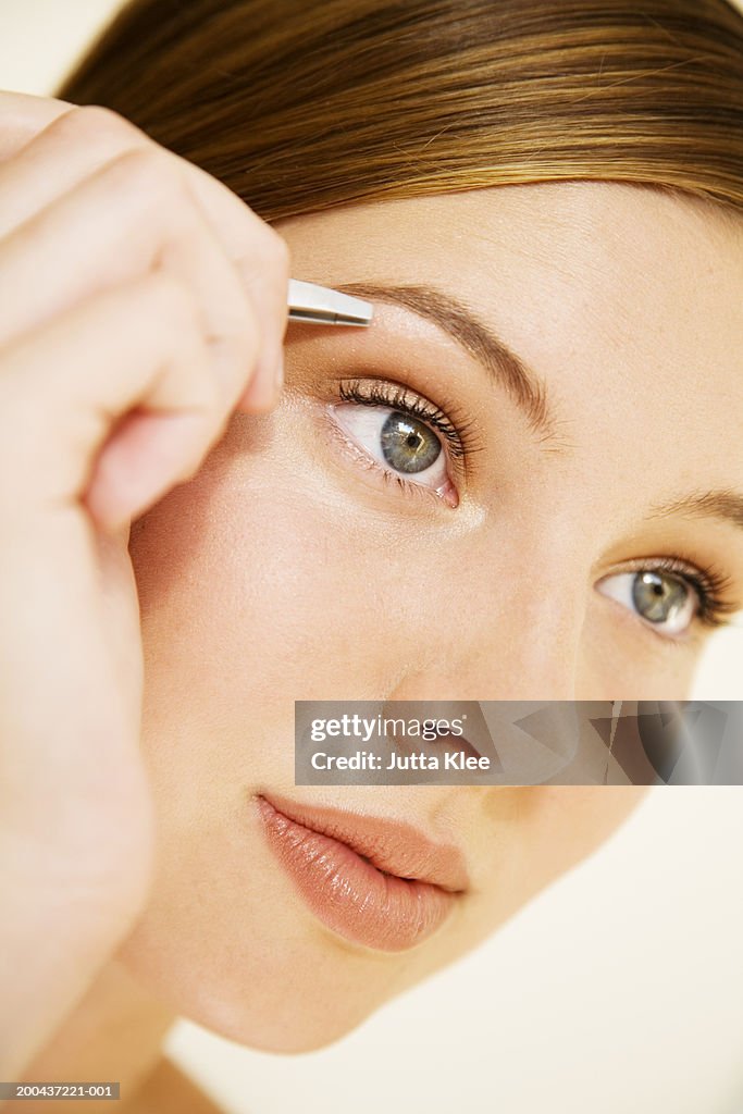 Young woman plucking eyebrow with tweezers, close-up