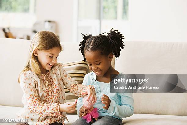 two girls (4-6) playing with doll in living room, smiling - puppe stock-fotos und bilder