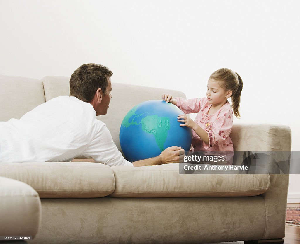 Father lying on sofa with daughter (4-6) holding globe