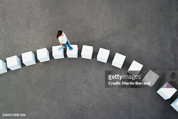 woman walking across line of giant white cubes, elevated view - stepping stone stock-fotos und bilder