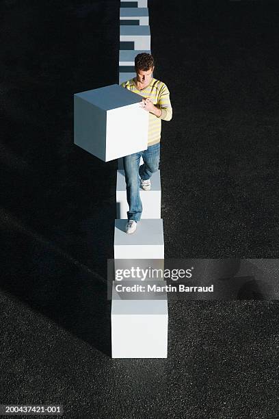 man walking across line of giant cubes, carrying giant cube - stepping stones stockfoto's en -beelden