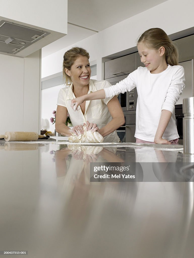 Mother and daughter (8-10) in kitchen, kneading dough