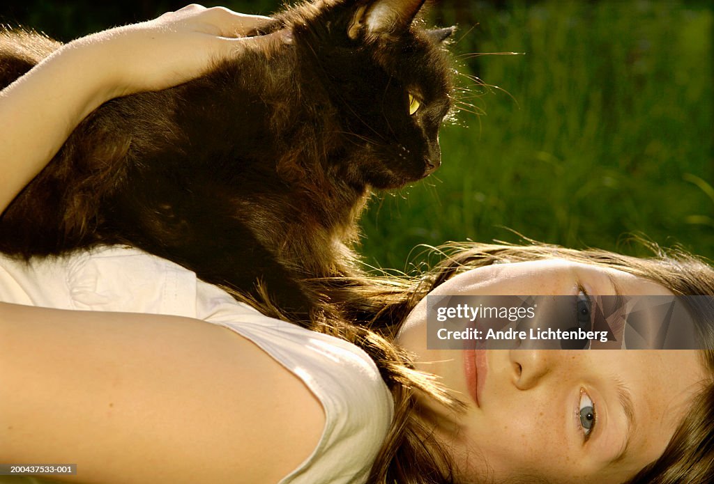 Girl (10-12) lying on ground with cat sitting on chest, portrait