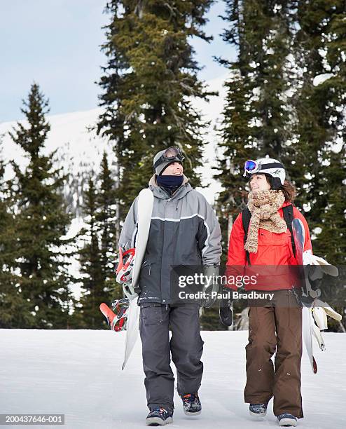 couple walking on snow, carrying snowboards, smiling - pantaloni da sci foto e immagini stock