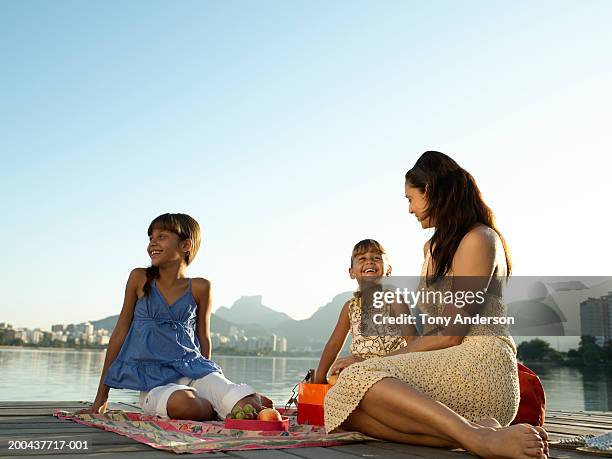 mother with daughters (4-9) having picnic on dock, smiling - women in see through dresses stock-fotos und bilder