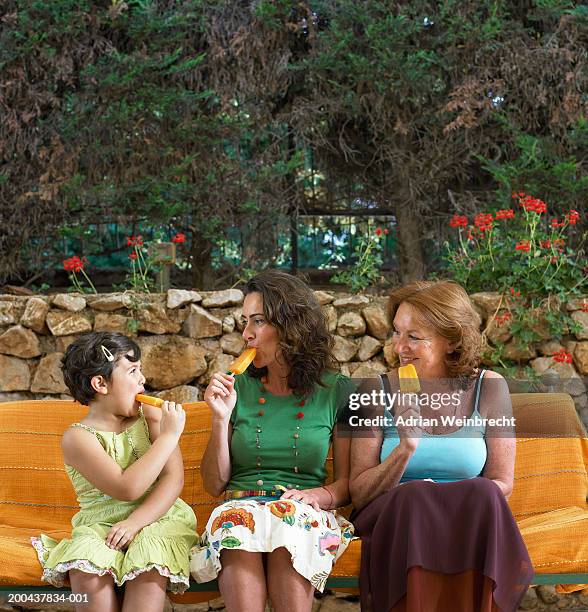 girl (5-7), mother and grandmother on garden bench, eating ice lollies - orange vest stock pictures, royalty-free photos & images