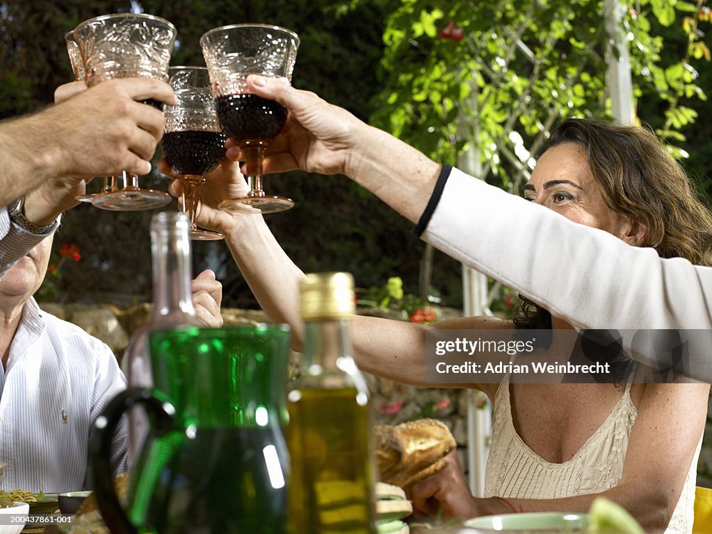 Group of people raising glasses at dinner table, outdoors