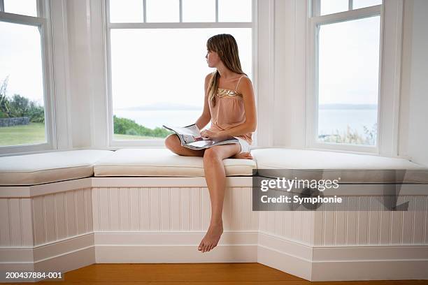 teenage girl (17-19) sitting in bay window with book, side view - janela saliente - fotografias e filmes do acervo