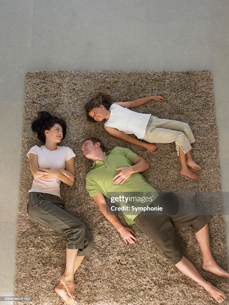 Parents and daughter (6-8) lying on carpet, elevated view