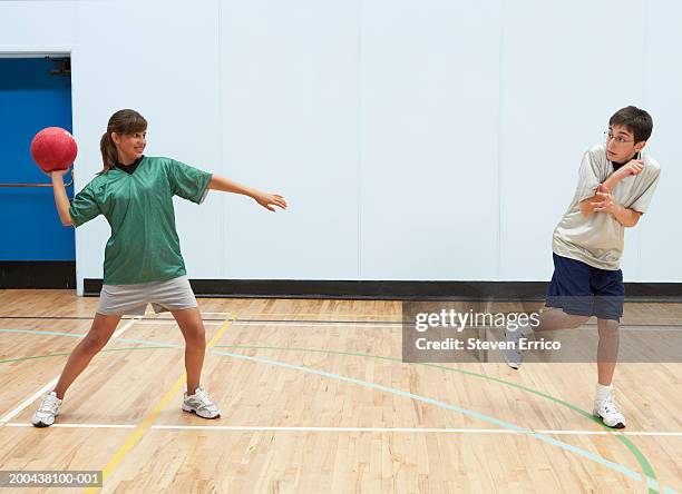 teenage boy and girl (12-14) playing dodge ball in school gymnasium - flip over stockfoto's en -beelden