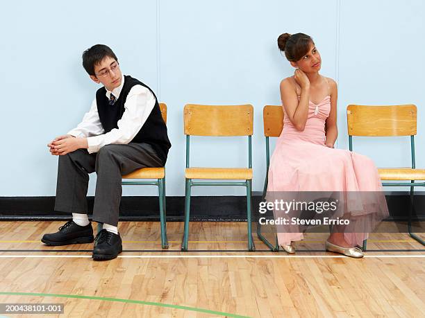 teenage boy and girl (12-14) sitting on chairs in gymnasium at dance - prom dress stockfoto's en -beelden