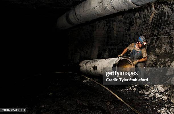 coal miner hauling ventilation tube throuh mine, side view - coal mine stock photos et images de collection